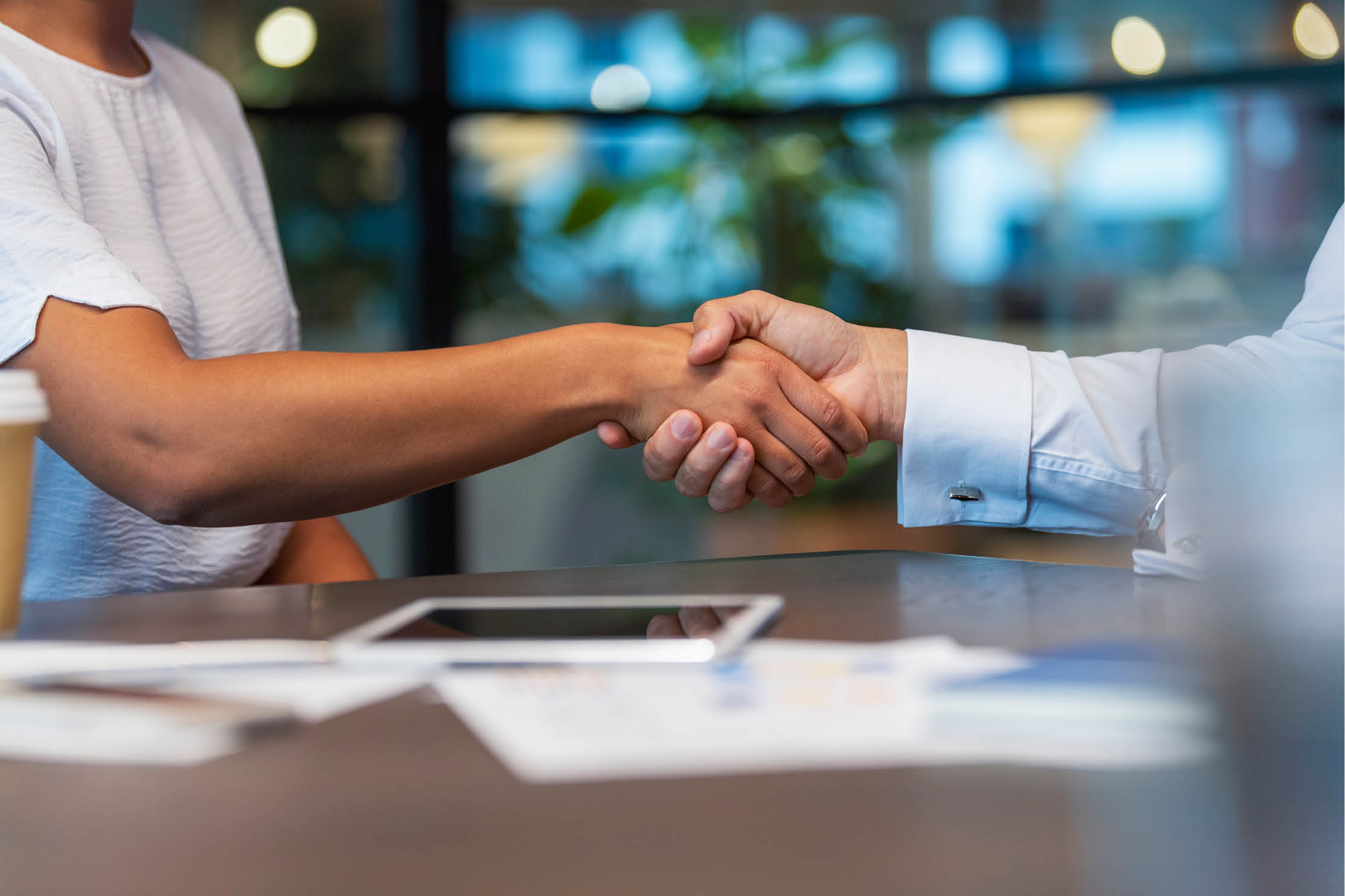 Business man and woman shaking hands in the office. There is a paperwork and technology on the table