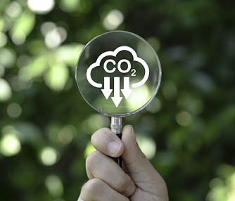 Hand holding magnifier glass with reduction carbon emission icon for zero carbon emission , CO2 carbon footprint and carbon credit to limit global warming within 2050 from Kyoto protocol concept.